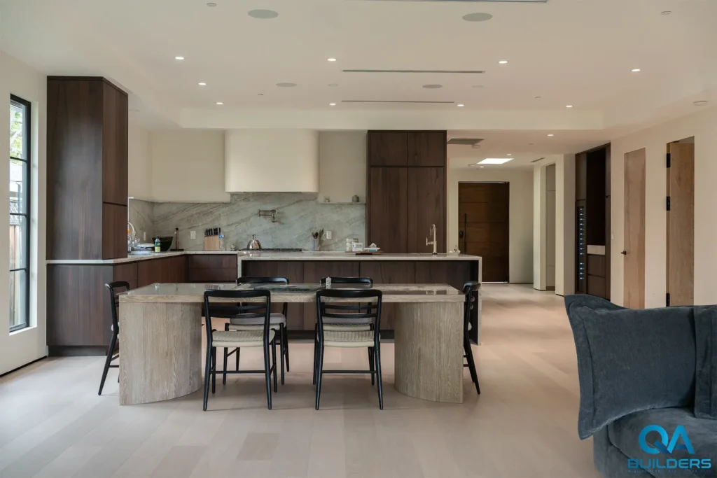 Stone dining table in front of a dark wood kitchen in an open plan with light floors, San Jose