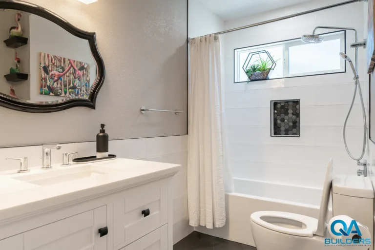 Bathroom with a white vanity, scalloped black mirror and a tub with a mosaic niche, San Jose