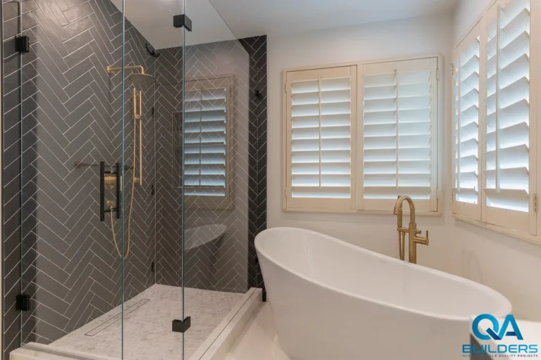 Glass shower with charcoal herringbone tile and gold-tone fixtures beside a freestanding tub, San Jose