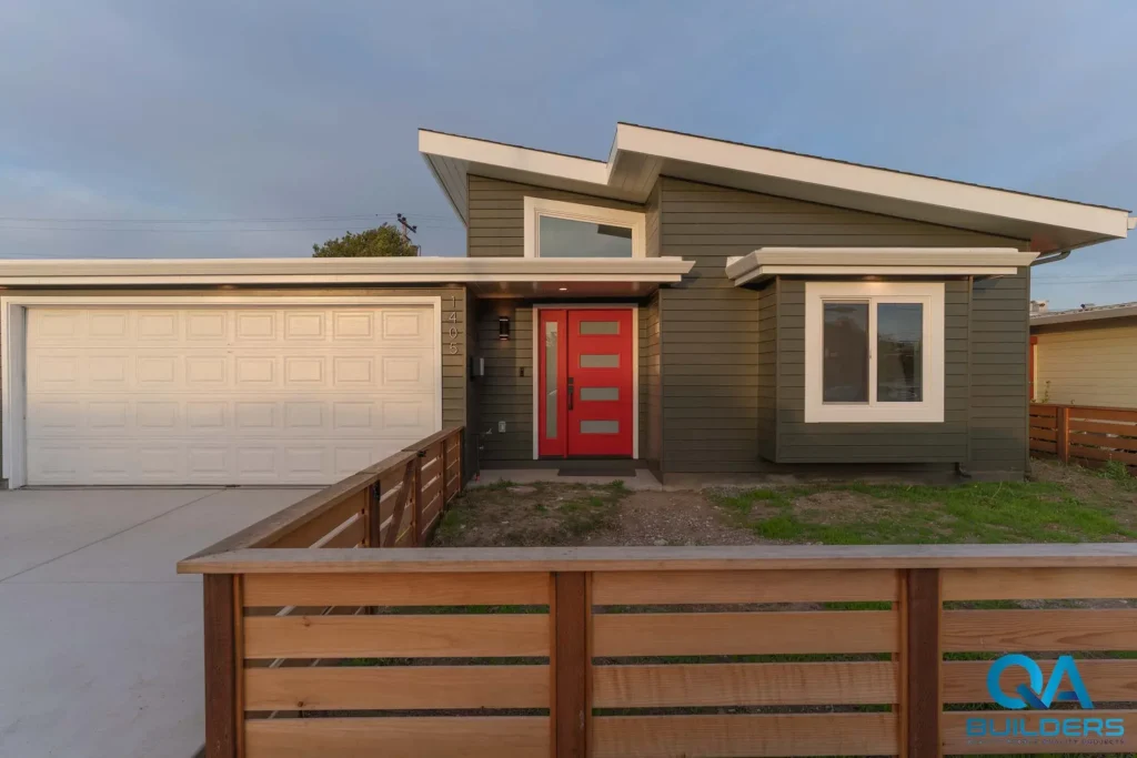 Front of the finished home with a red door, dark siding and a wood fence, San Mateo