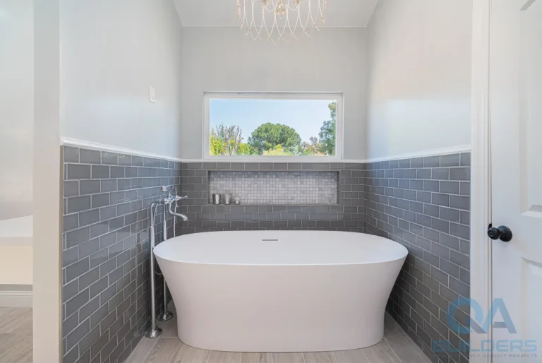 Freestanding tub against gray subway tile under a picture window, San Jose