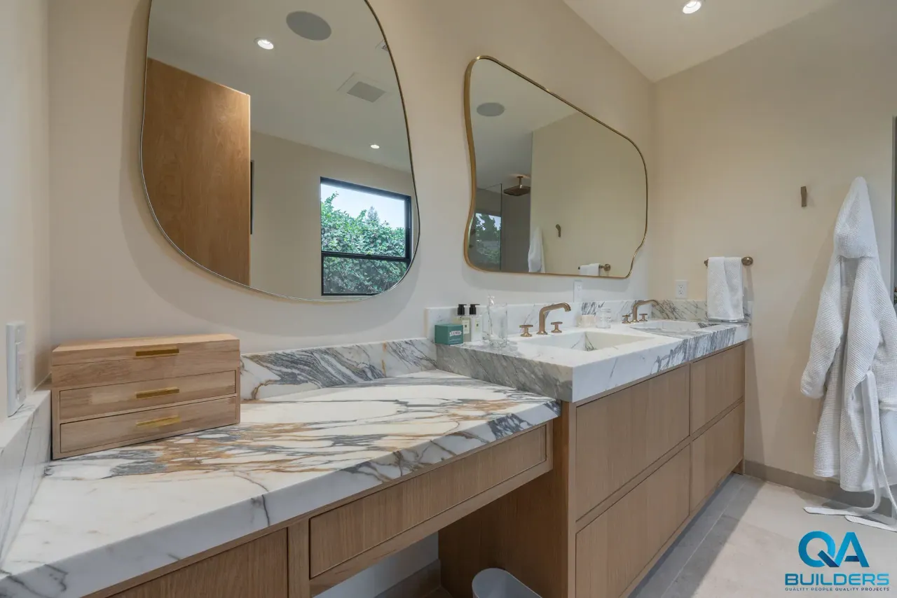 Light wood double vanity with a gold-veined marble-look top under two curved mirrors, San Jose