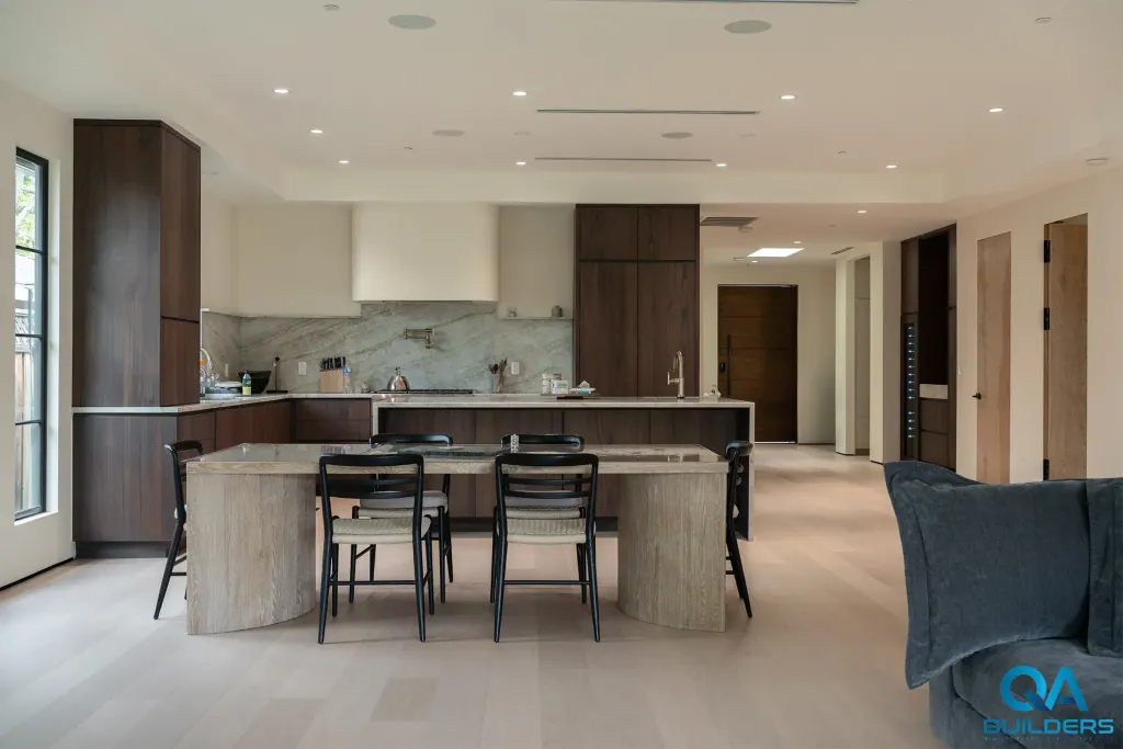Stone dining table in front of a dark wood kitchen in an open plan with light floors, San Jose